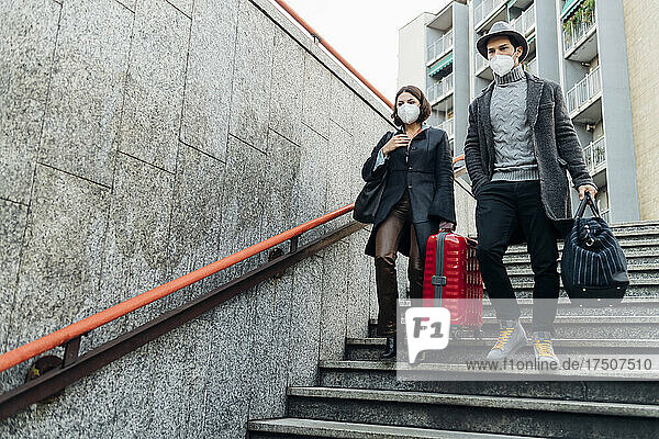 Young man and woman with luggage walking down on staircase during pandemic