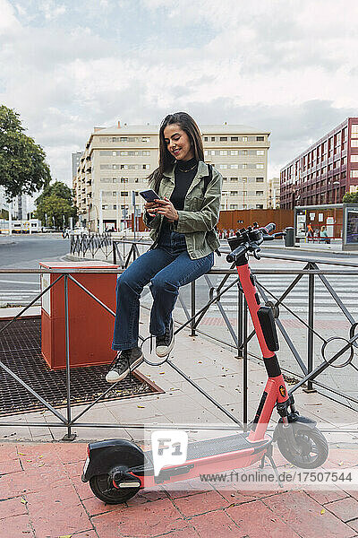 Junge Frau benutzt Mobiltelefon am Geländer in der Stadt