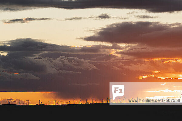 Dramatic sunset over silhouettes of distant wind farm turbines