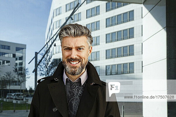 Smiling bearded businessman standing in front of building