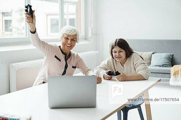 Cheerful grandmother and granddaughter playing video game at home