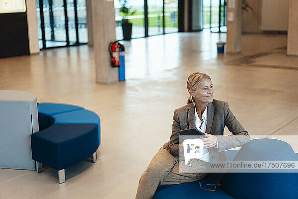 Smiling businesswoman with tablet PC sitting in office lobby