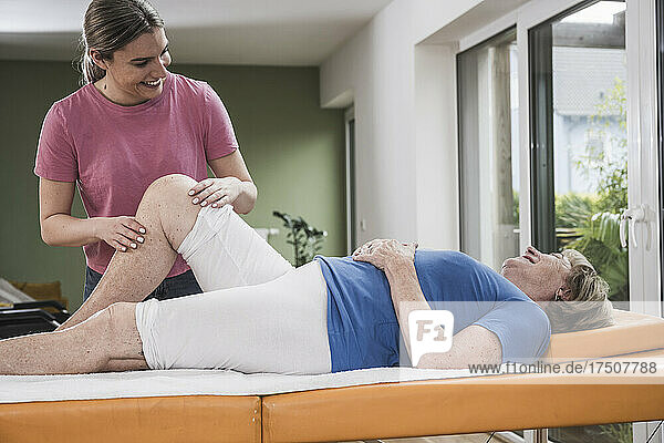 Smiling physiotherapist massaging disabled woman's knee on massage table