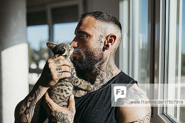 Man with tattoo kissing cat at home