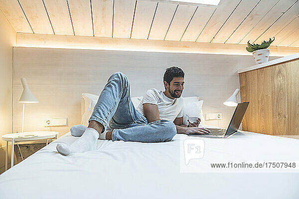 Smiling freelancer lying on bed using laptop