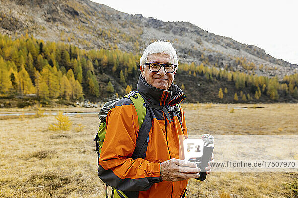 Smiling senior hiker holding insulated drink container at Rhaetian Alps  Italy