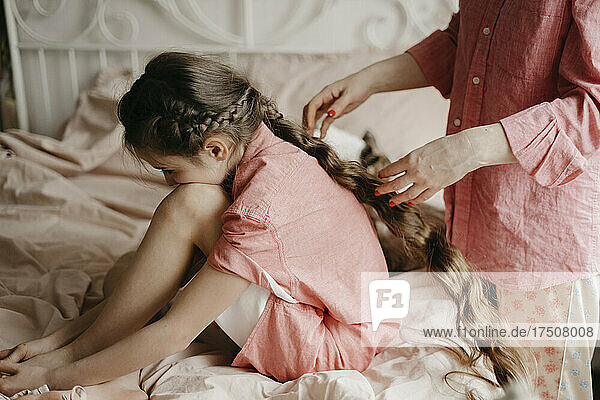 Woman braiding daughter's hair in bedroom