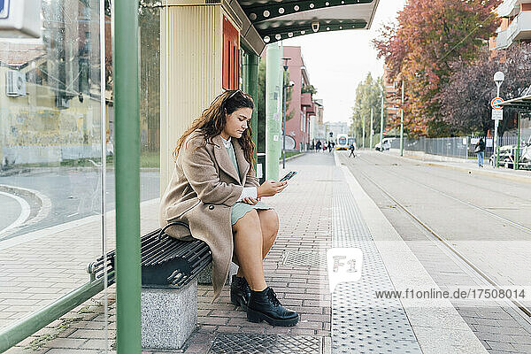 Voluptuous woman using mobile phone while waiting at tram station