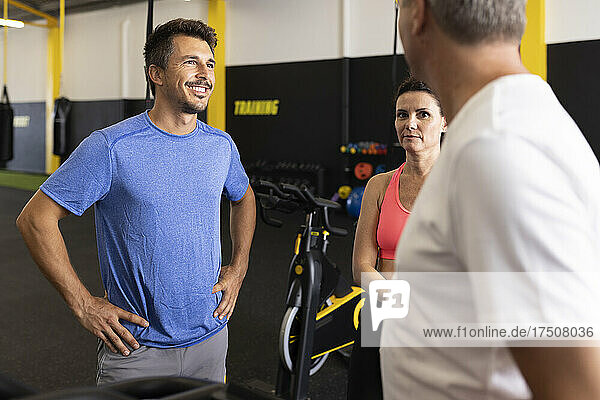 Smiling sportsman with hand on hip talking with friends in gym