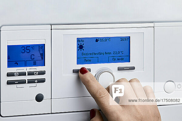 Woman adjusting control panel of heating boiler at home