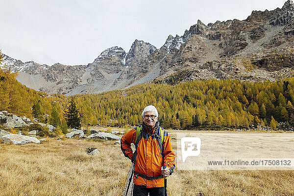 Lächelnder Tourist mit Wanderstöcken inmitten von Gras in den Rhätischen Alpen  Italien