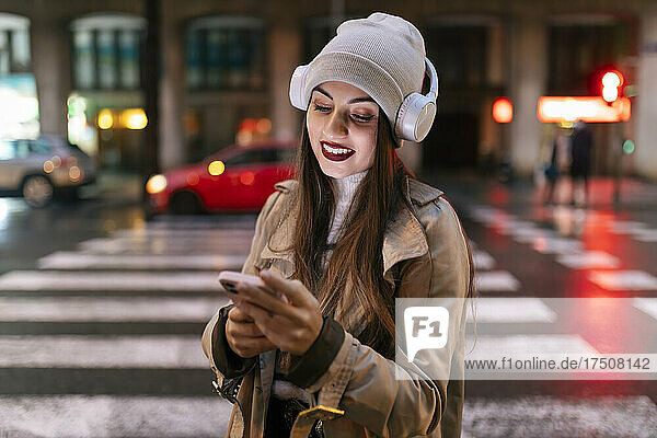 Young woman with headphones using smart phone in city