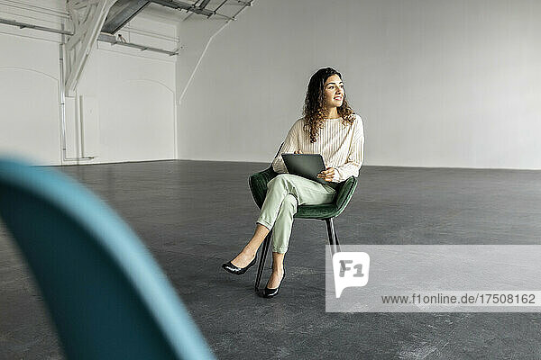 Smiling businesswoman with graphics tablet sitting on chair at industrial hall