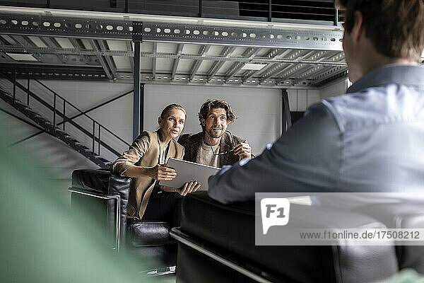 Businesswoman with tablet pc discussing with businessman by colleague in lobby