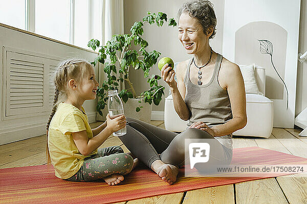 Smiling mother and daughter having food and drink on exercise mat