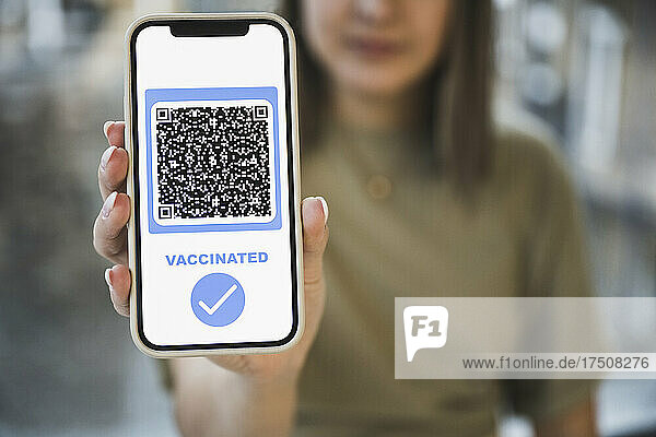 Woman showing vaccinated QR code with check mark symbol on mobile screen