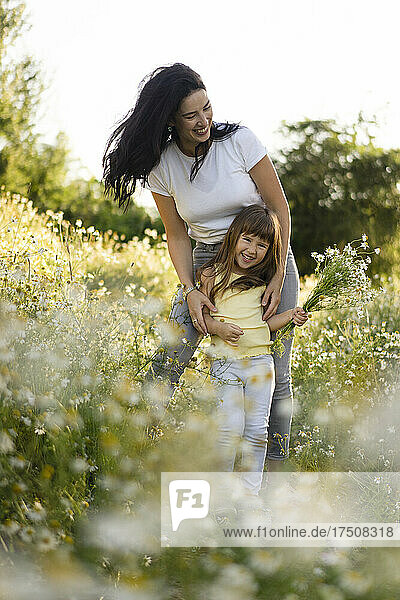 Mother playing with daughter holding bunch of flowers in meadow