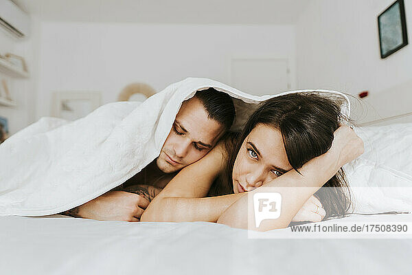 Man leaning on woman under duvet in bedroom