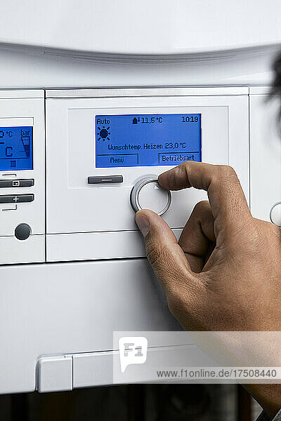 Man adjusting heating boiler with control knob at home
