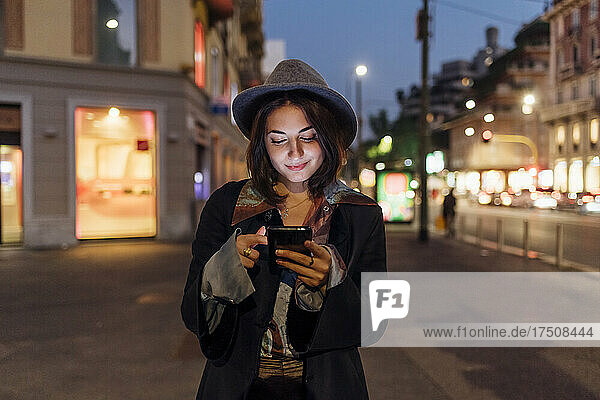 Smiling young woman using smart phone on city street