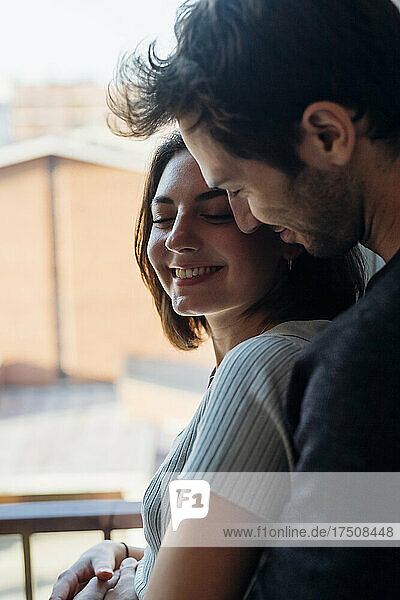 Smiling young couple standing by window at home