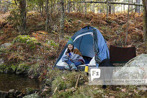 Smiling woman having coffee in tent at autumn forest