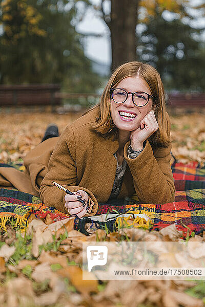 Happy woman lying on blanket in autumn park