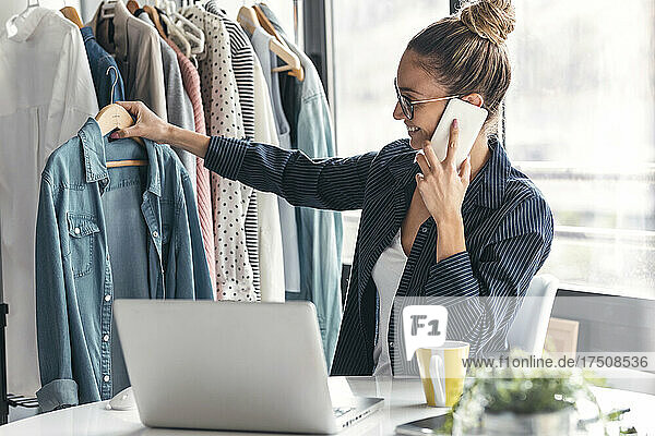 Fashion designer holding shirt and talking on mobile phone in office