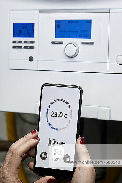 Woman adjusting temperature of heating boiler through mobile phone at home