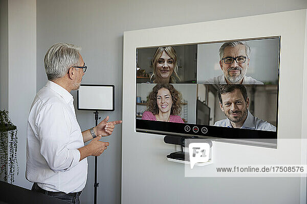 Mature businessman talking on video conference through television in office
