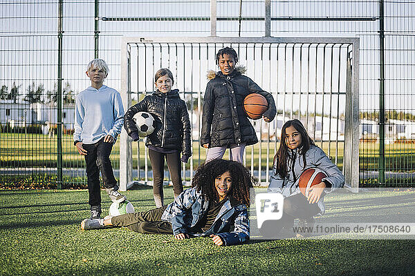 Porträt von Mädchen und Jungen mit Sportbällen auf einem Fußballplatz