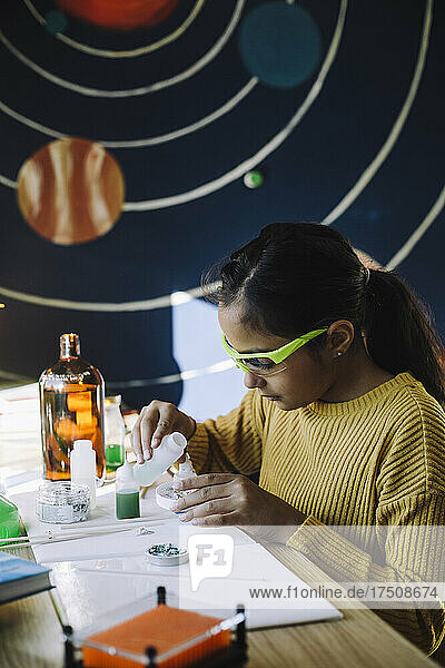 Motiviertes Mädchen gießt Chemikalien ein  während sie ein wissenschaftliches Experiment am Tisch durchführt