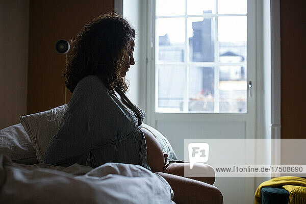 Pregnant woman sitting on bed in bedroom