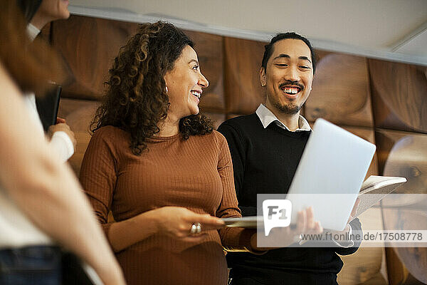 Happy businesswoman discussing over laptop with male and female colleagues in office