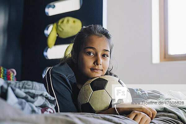 Porträt eines Mädchens mit Fußball  das zu Hause auf dem Bett liegt