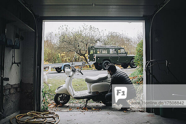 Erwachsener Mann repariert Motorroller in einer Garage