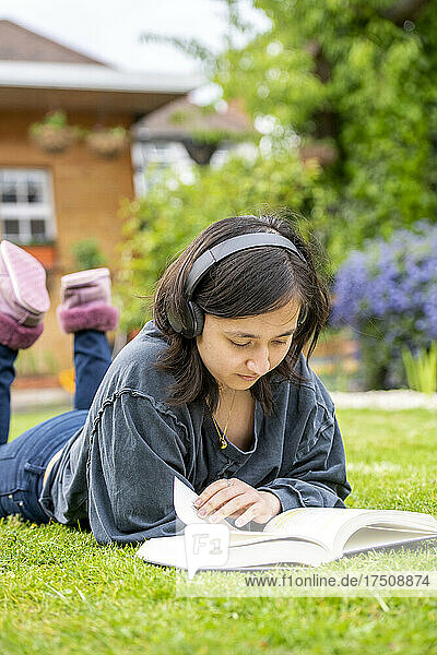 Young woman with headphones reading book in garden