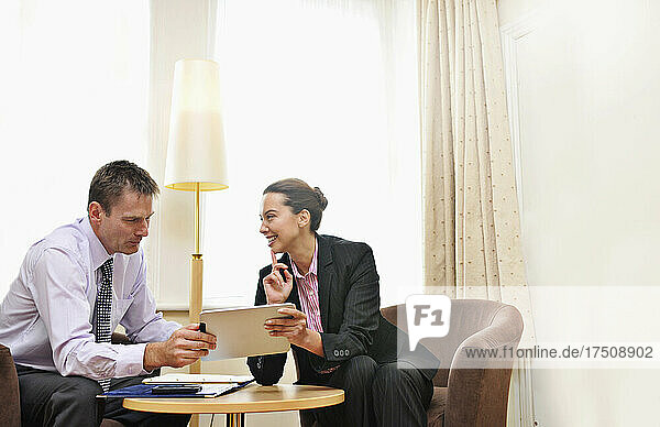 Eine Geschäftsfrau und ein Mann treffen sich in einer Hotellobby oder einem Zimmer und schauen auf ein ipad.