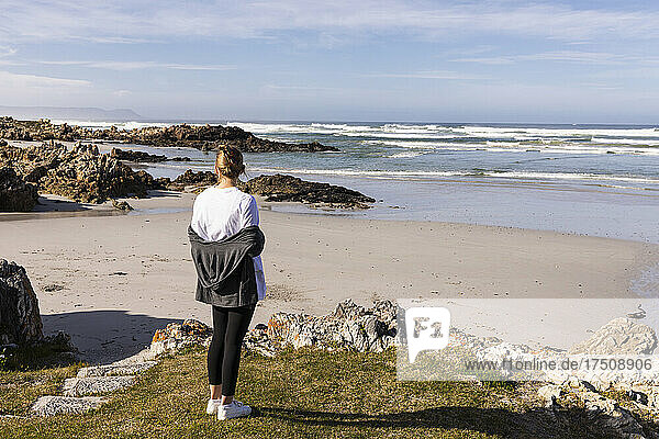 Teenager-Mädchen steht auf Felsen mit Blick auf einen Sandstrand