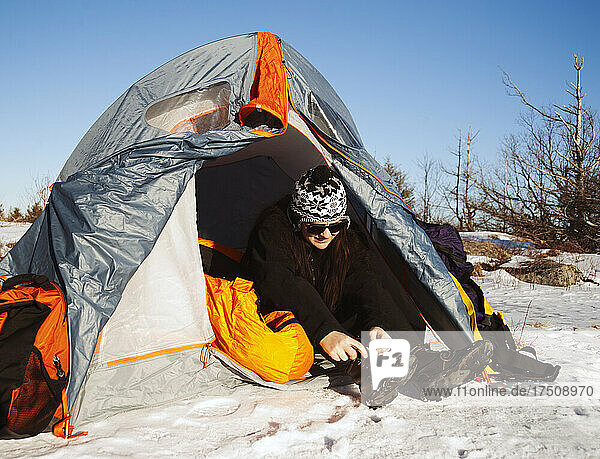 Woman sitting in tent in snowy landscape lacing up snow boots.
