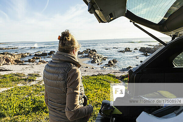 Adult woman by the open door of a vehicle at the beach getting ready for hiking.