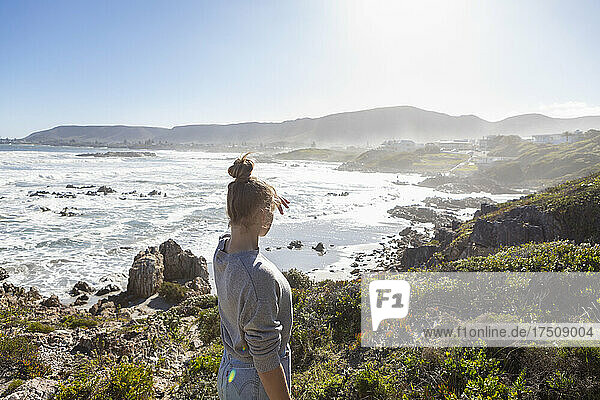 A teenage girl on rocks  looking at the coastline  waves breaking and mist rising.