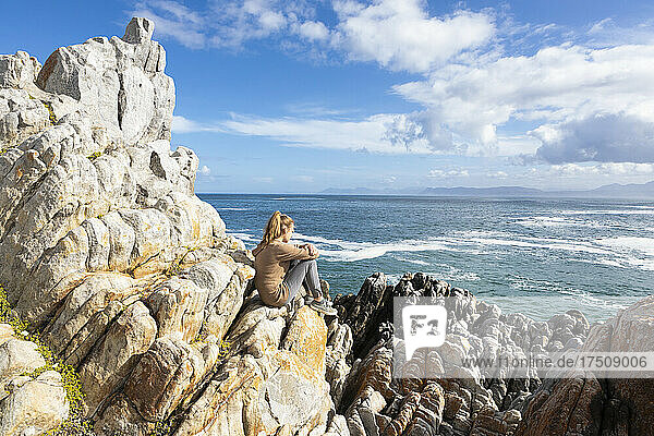 Teenager-Mädchen sitzt auf einem Felsen und blickt auf den Atlantik und die Küste