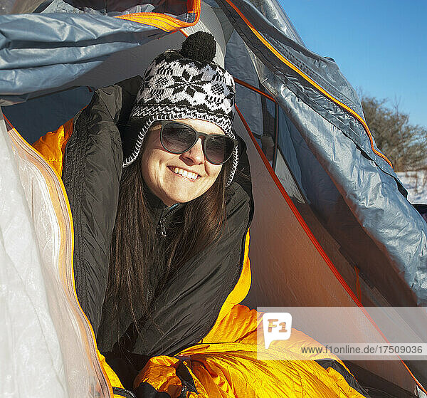 Frau schaut lächelnd aus der Zeltklappe und trägt eine Wintermütze.