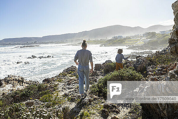 Teenage girl and a young boy walking along a coastal path above the ocean.