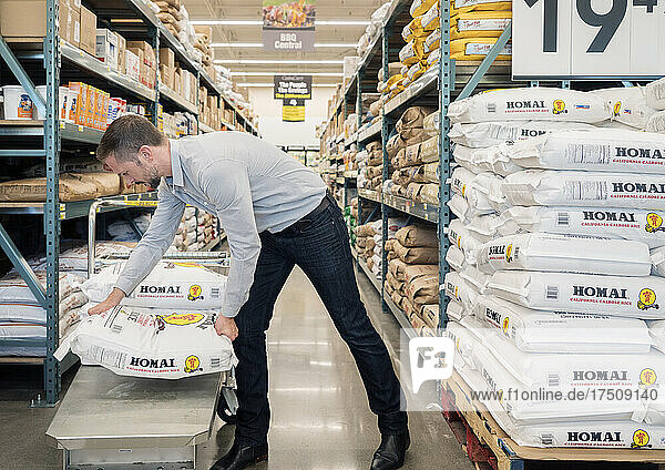 Ein Mann lädt einen Sack mit Lebensmitteln auf einen Einkaufswagen in einem Großhandelsgeschäft.