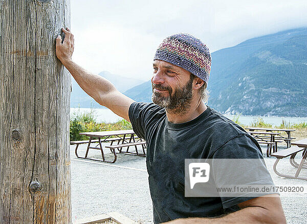 Man at picnic area among mountains wearing knitted hat.