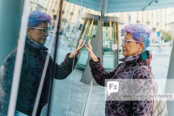 Italy  Fashionable senior woman touching glass surface in city