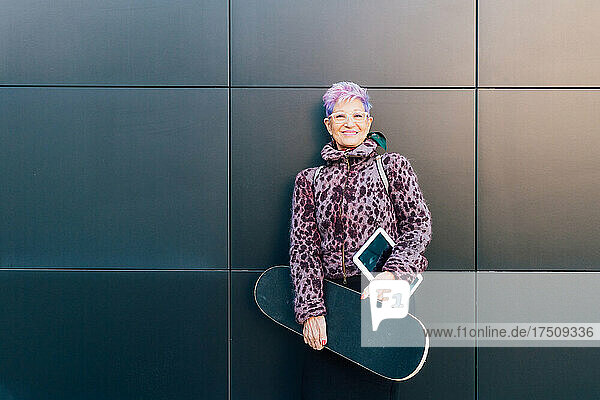 Italy  Portrait of fashionable senior woman with skateboard and digital tablet