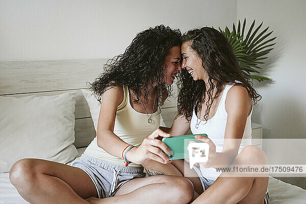 Fröhliches lesbisches Paar macht ein Selfie mit dem Smartphone  während es zu Hause im Bett sitzt
